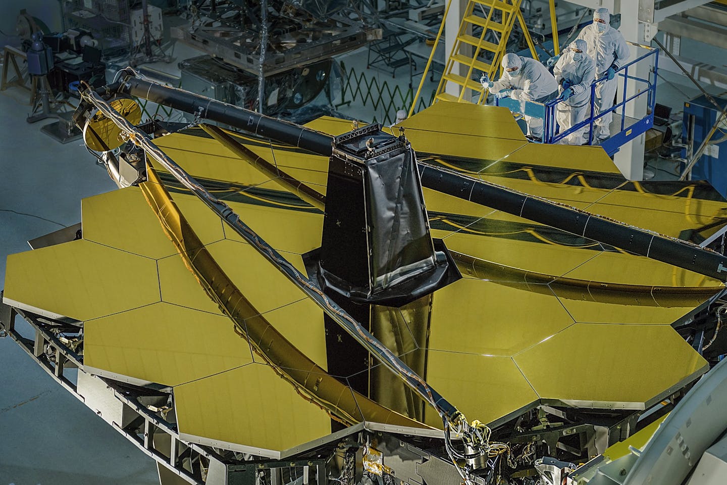 A moody image of the honeycomb-like mirror layout still in a lab with people in protective gear inspecting it.