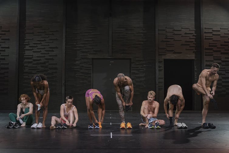 A line of dancers put on sneakers.