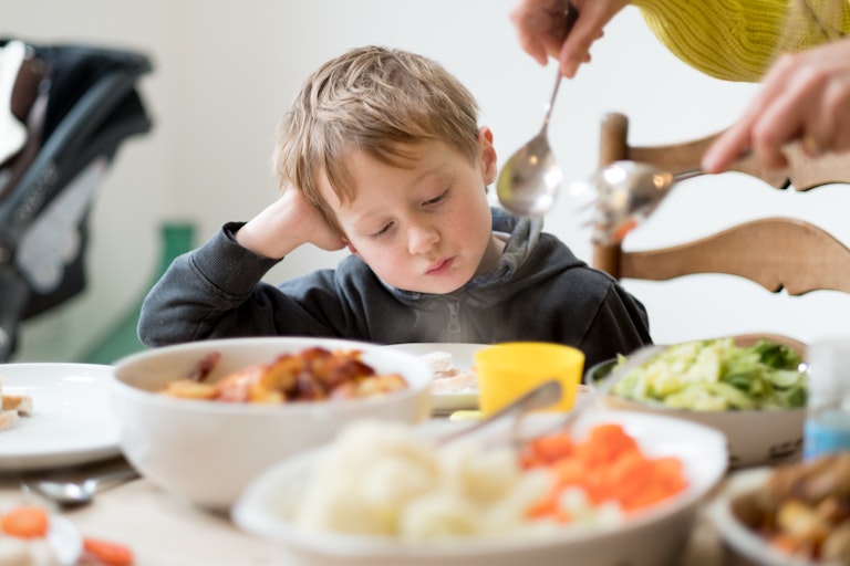 Boy watches as adult serves him vegetables