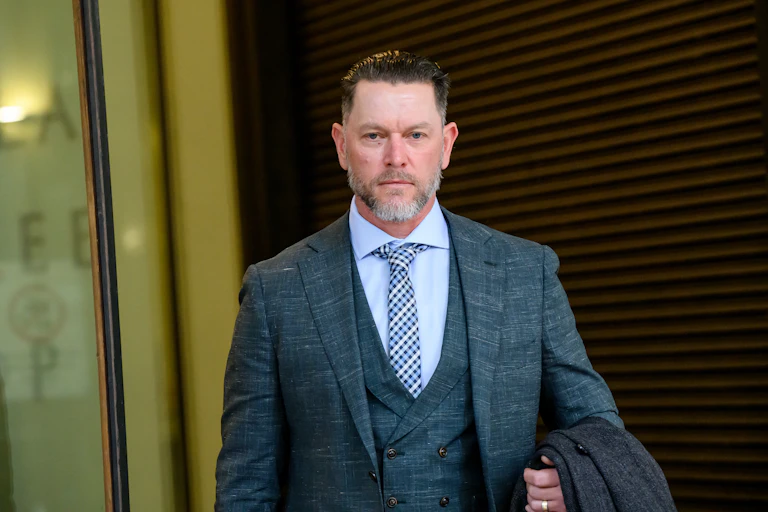 A man in a suit and waistcoat walks out of a building