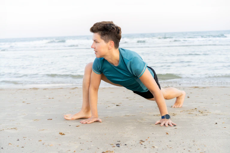 A woman crawls on all four limbs across a sandy beach.