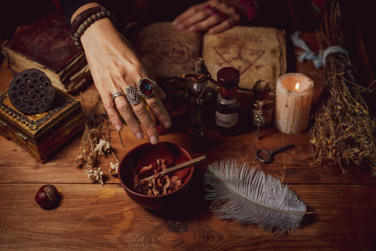 Female witch making potion on dark background, magic bottles with potions and candles on table of alchemist