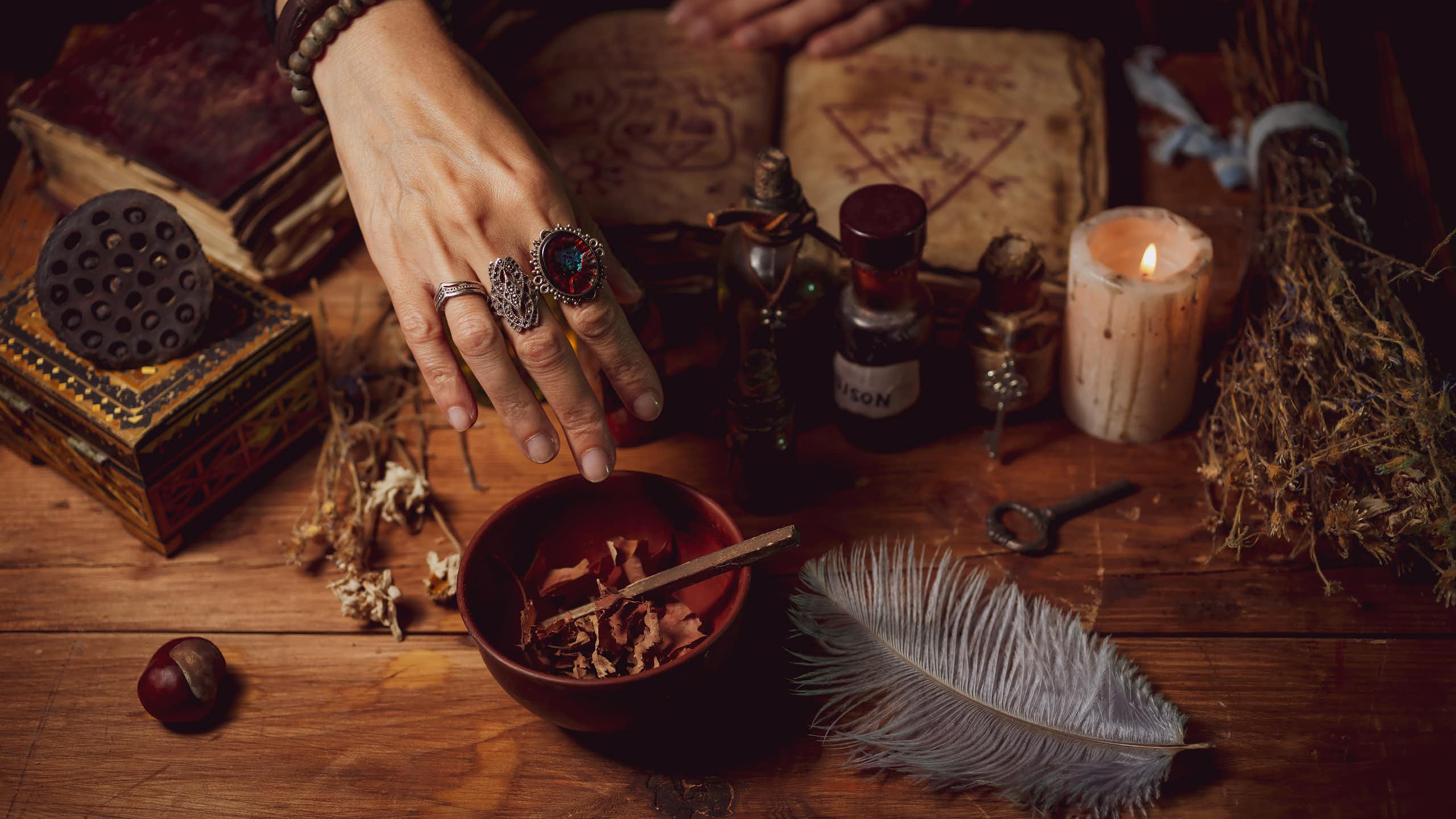 Female witch making potion on dark background, magic bottles with potions and candles on table of alchemist