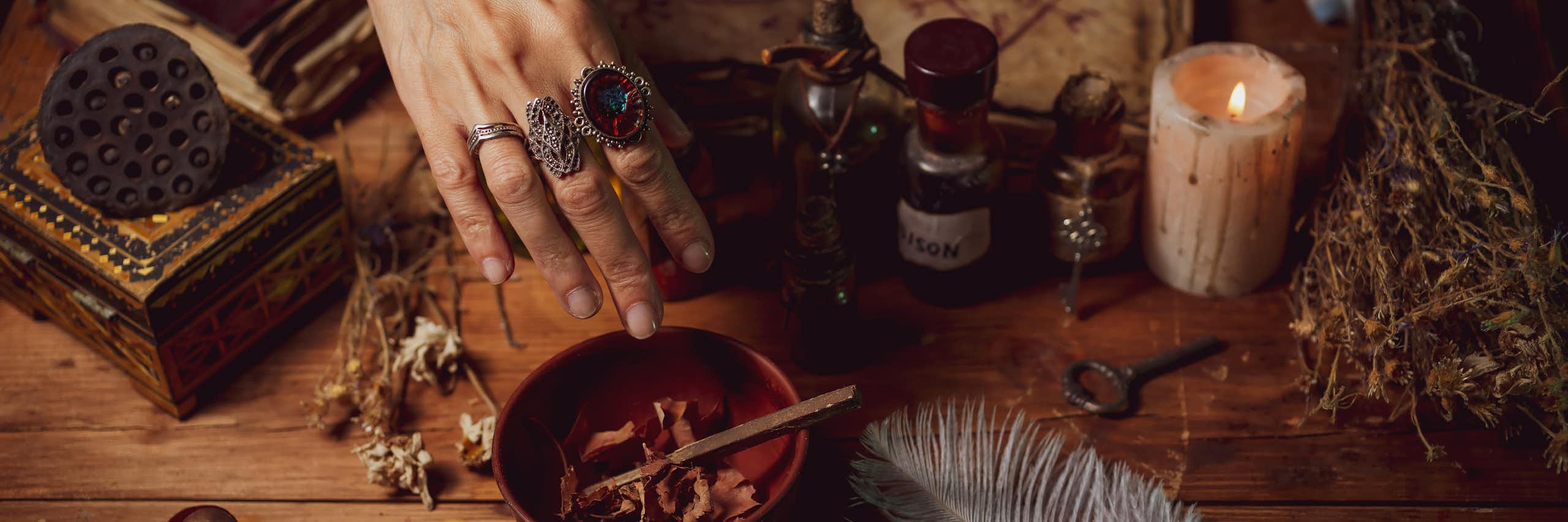 Female witch making potion on dark background, magic bottles with potions and candles on table of alchemist