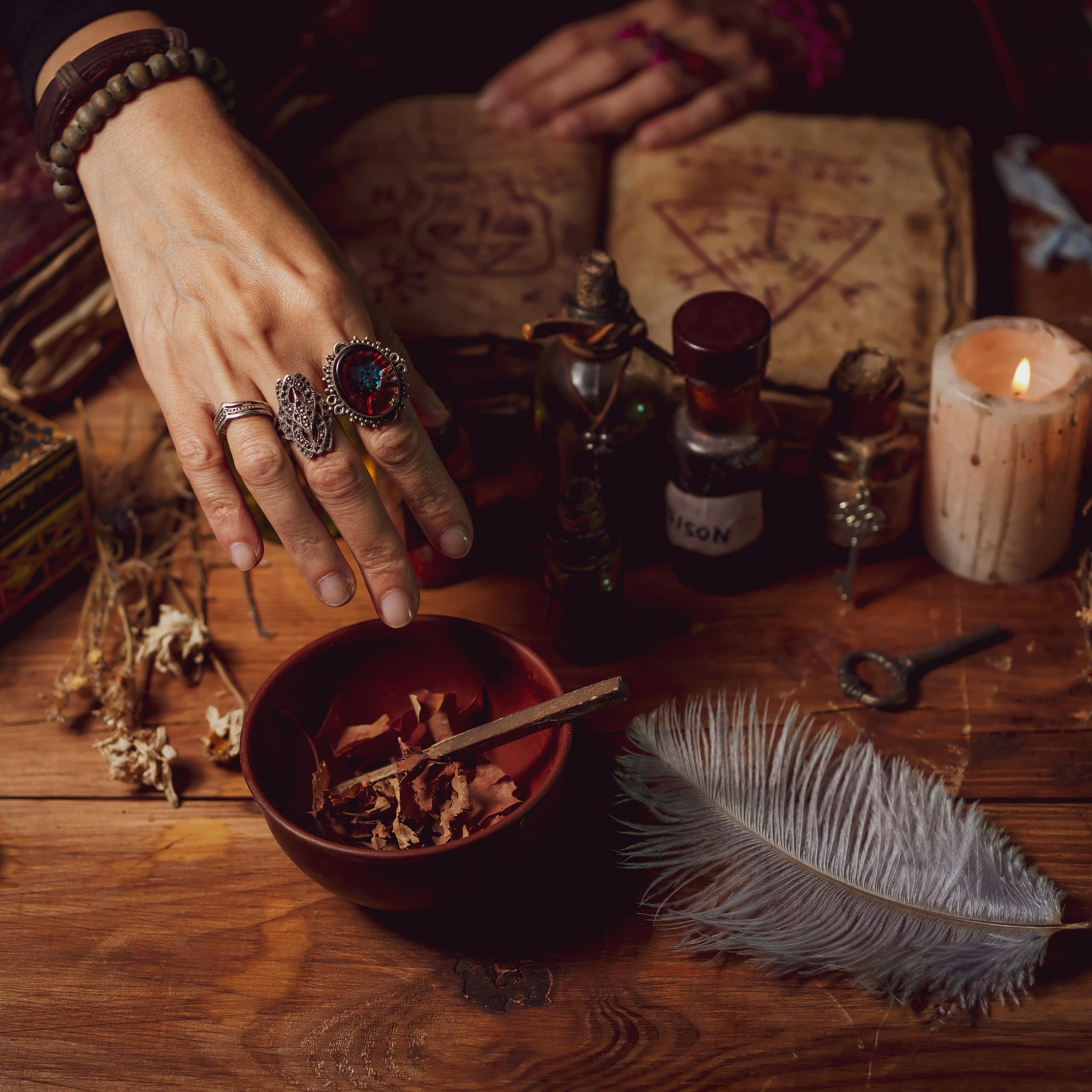 Female witch making potion on dark background, magic bottles with potions and candles on table of alchemist