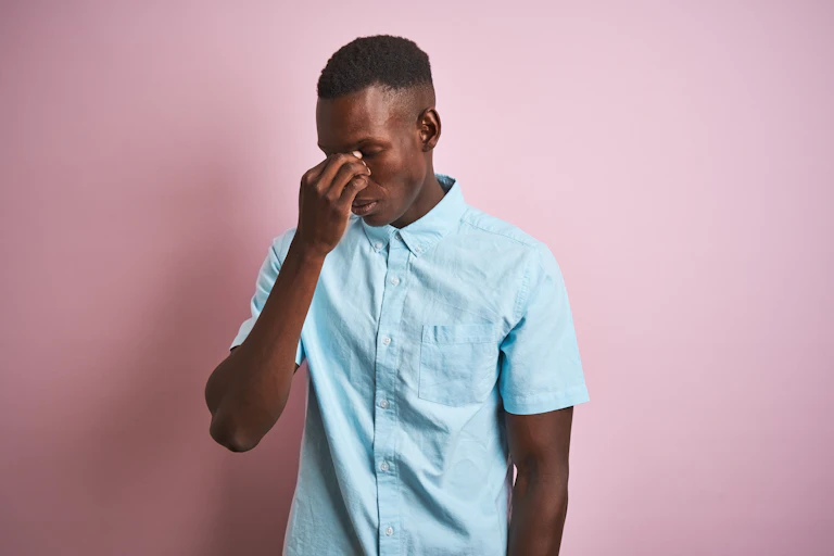 A young man holds the bridge of his nose, seeming to suffer from a headache.