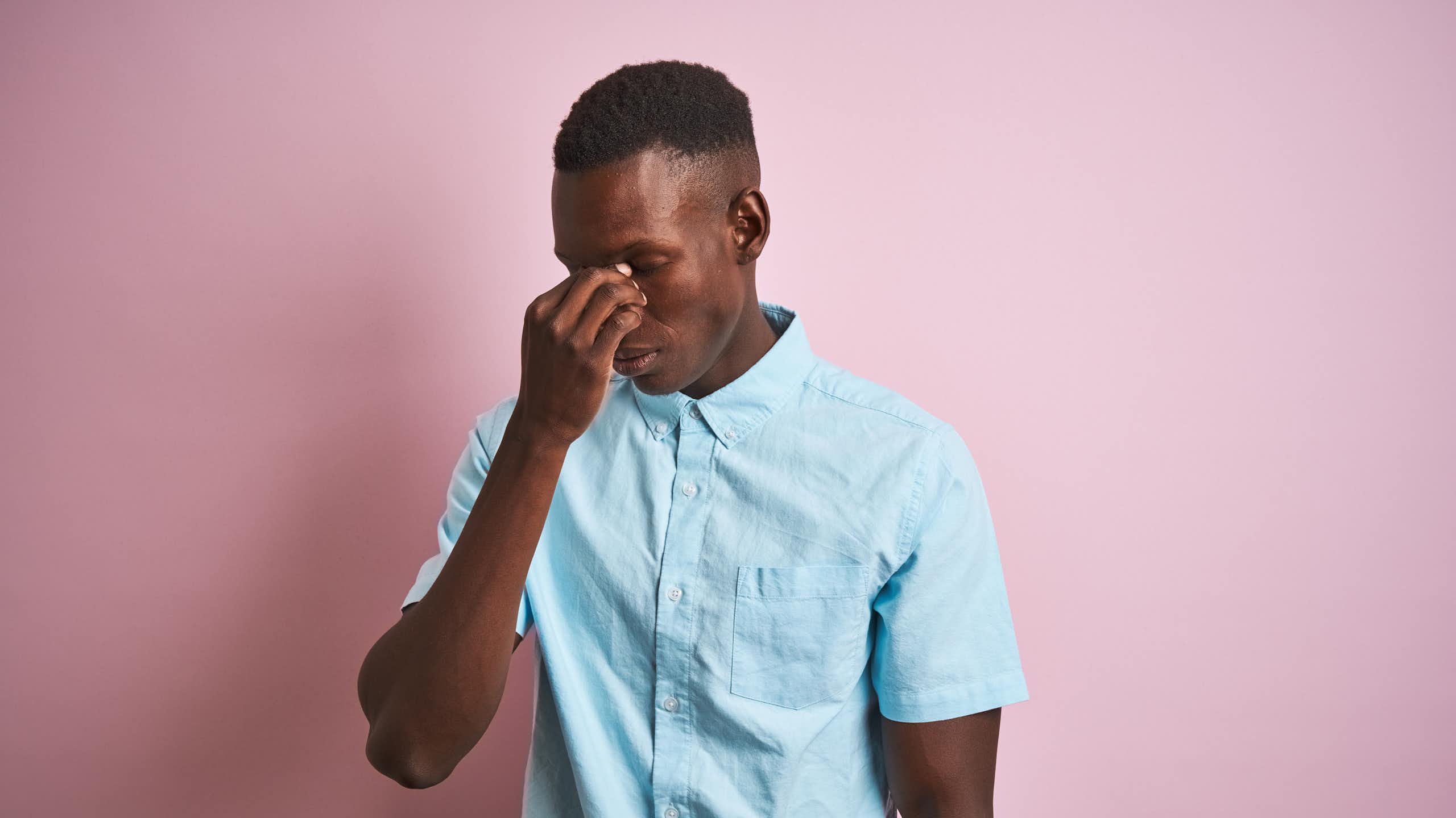 A young man holds the bridge of his nose, seeming to suffer from a headache.