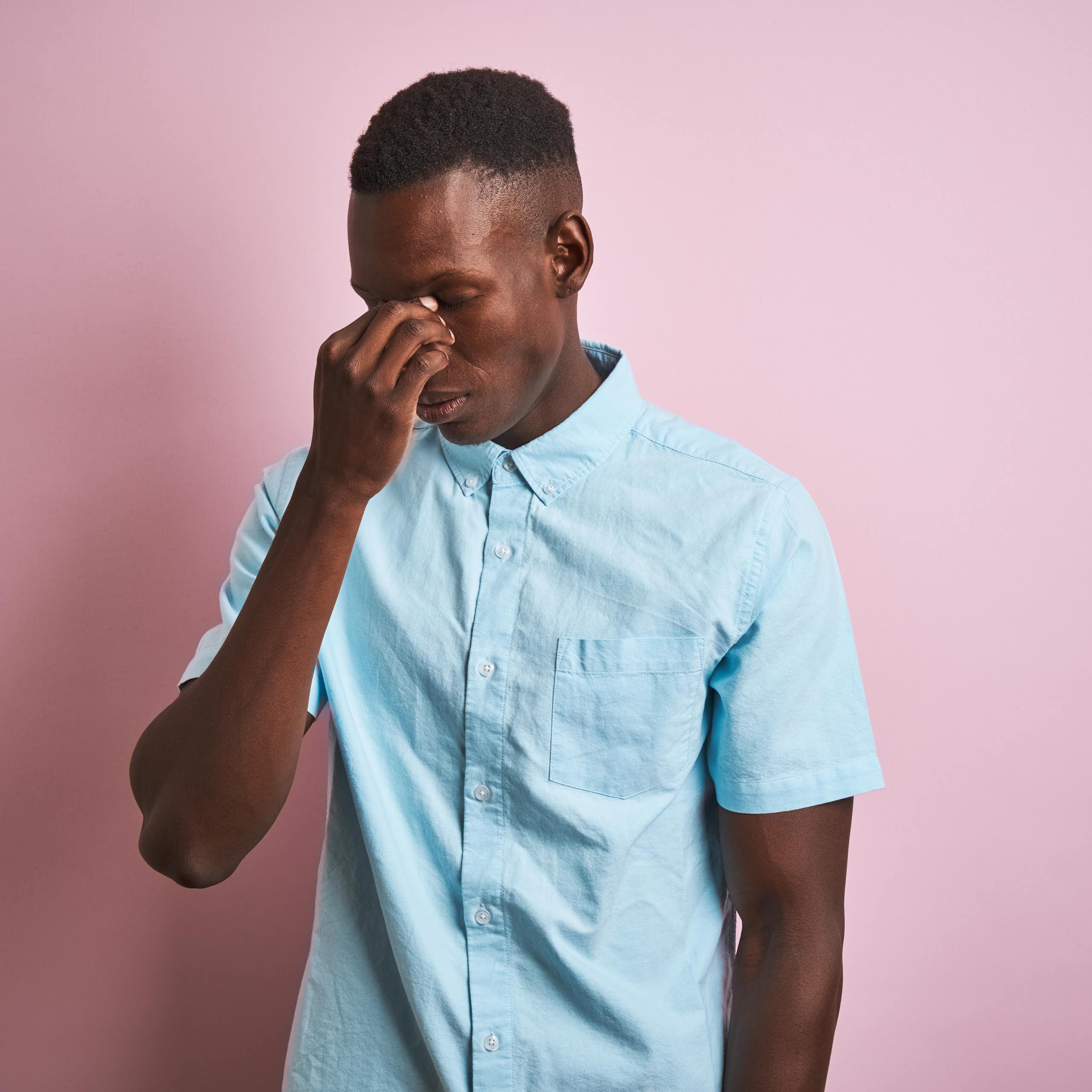 A young man holds the bridge of his nose, seeming to suffer from a headache.