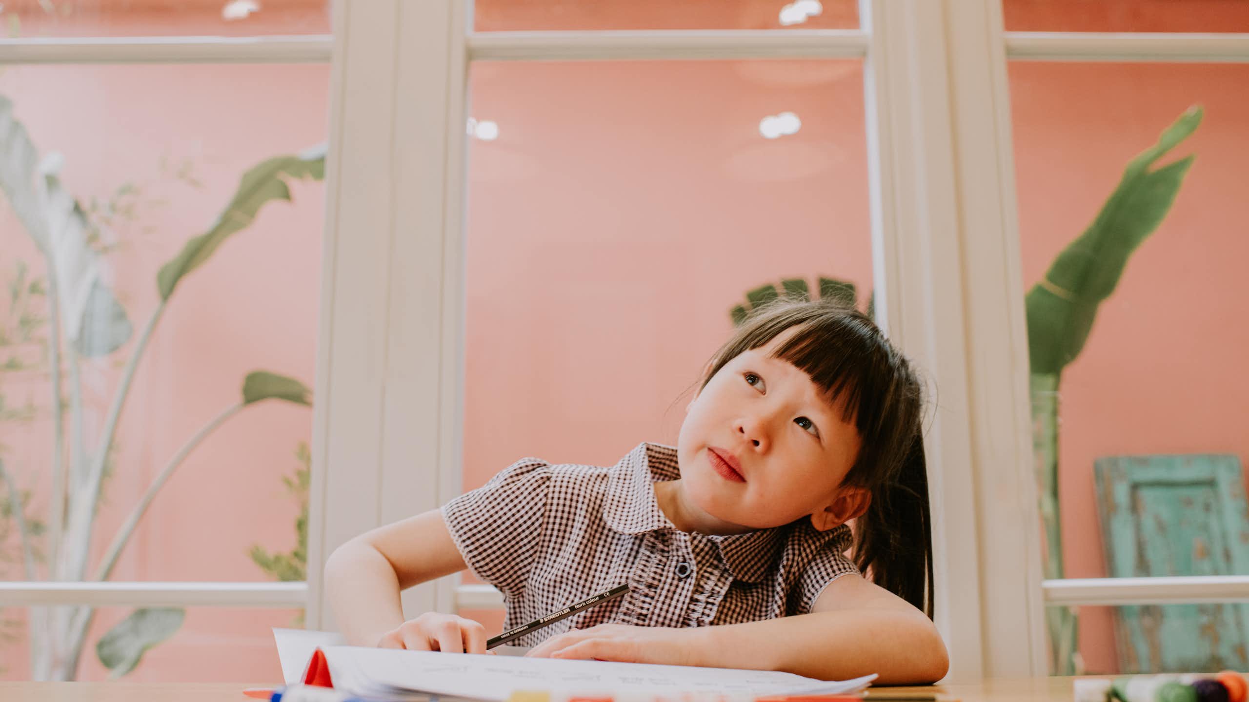 Young child sitting at a table and looking up toward the sky as if daydreaming.