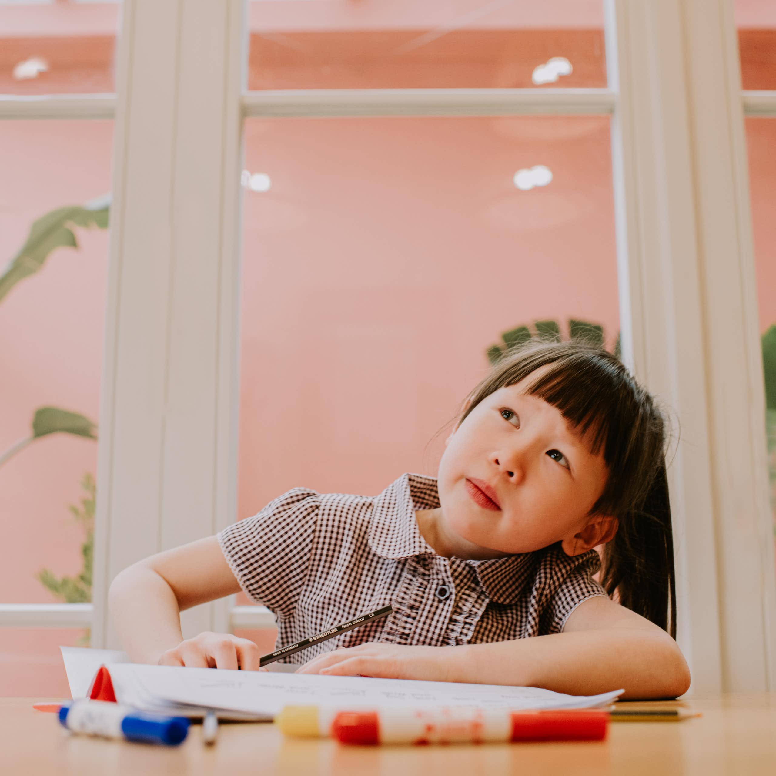 Young child sitting at a table and looking up toward the sky as if daydreaming.