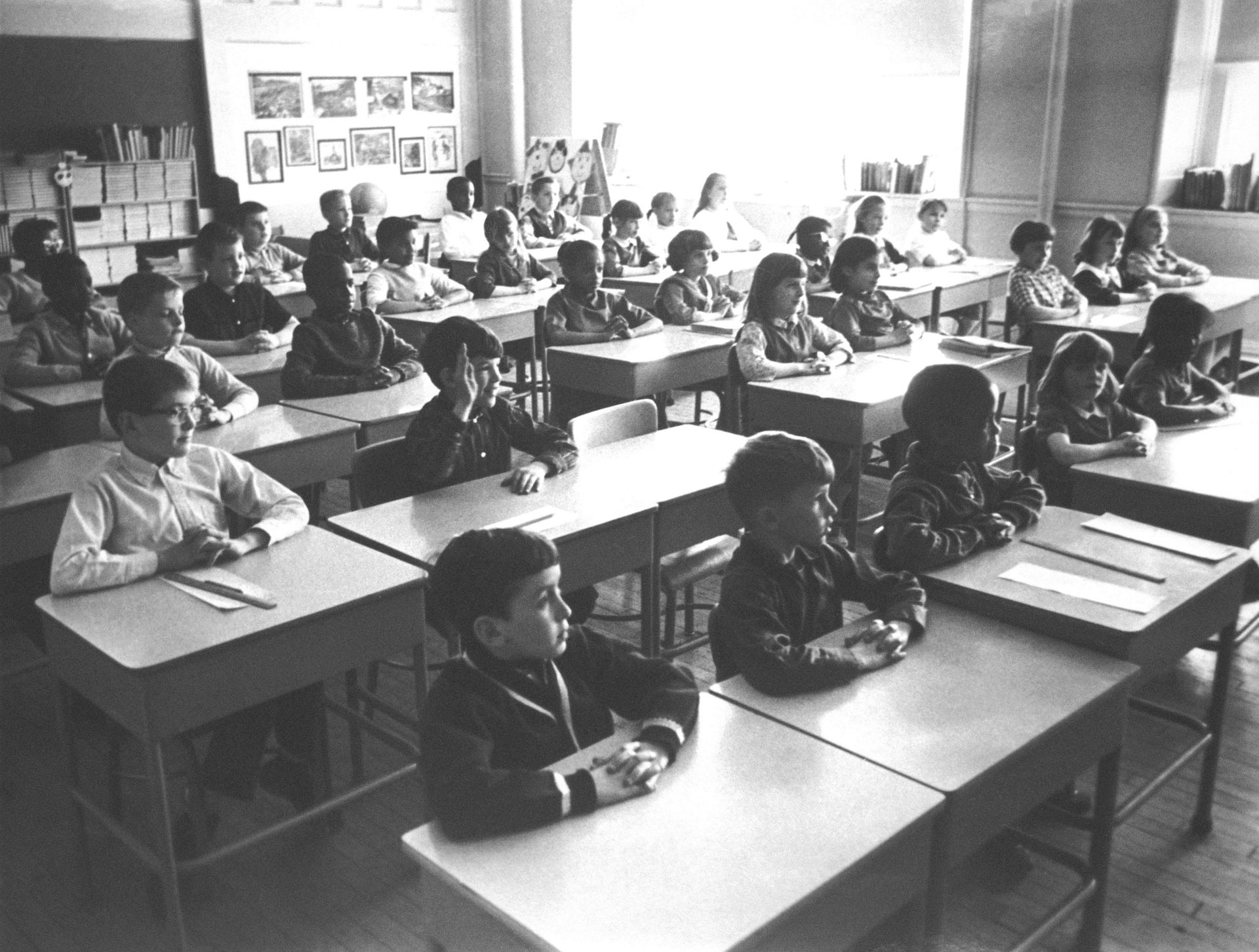 Black-and-white photo of elementary school children seated at desks in classroom