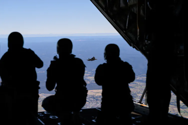The silhouettes of three soldiers in a fighter plane in the air