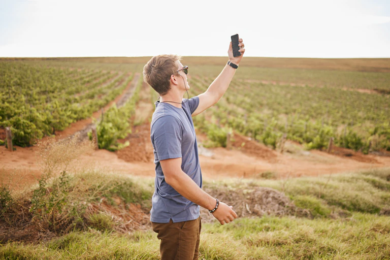 A young man holding a phone up to the sky in the middle of a field.