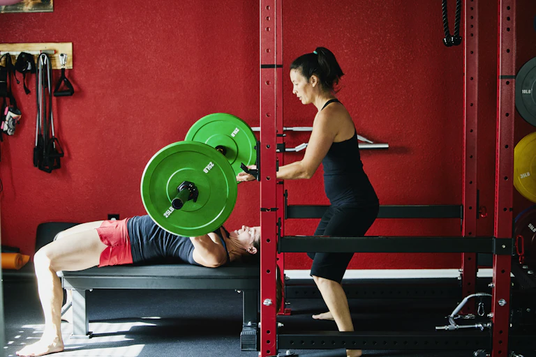 Woman spots man lying on back as he lifts weights over neck.