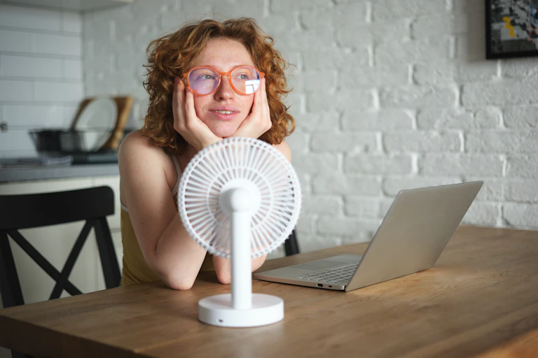 Woman in early menopause hits her face in her hands and cools down with a fan