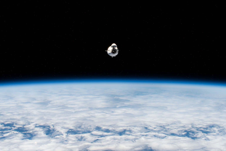 A small white capsule flying above a blue planet against a black void.