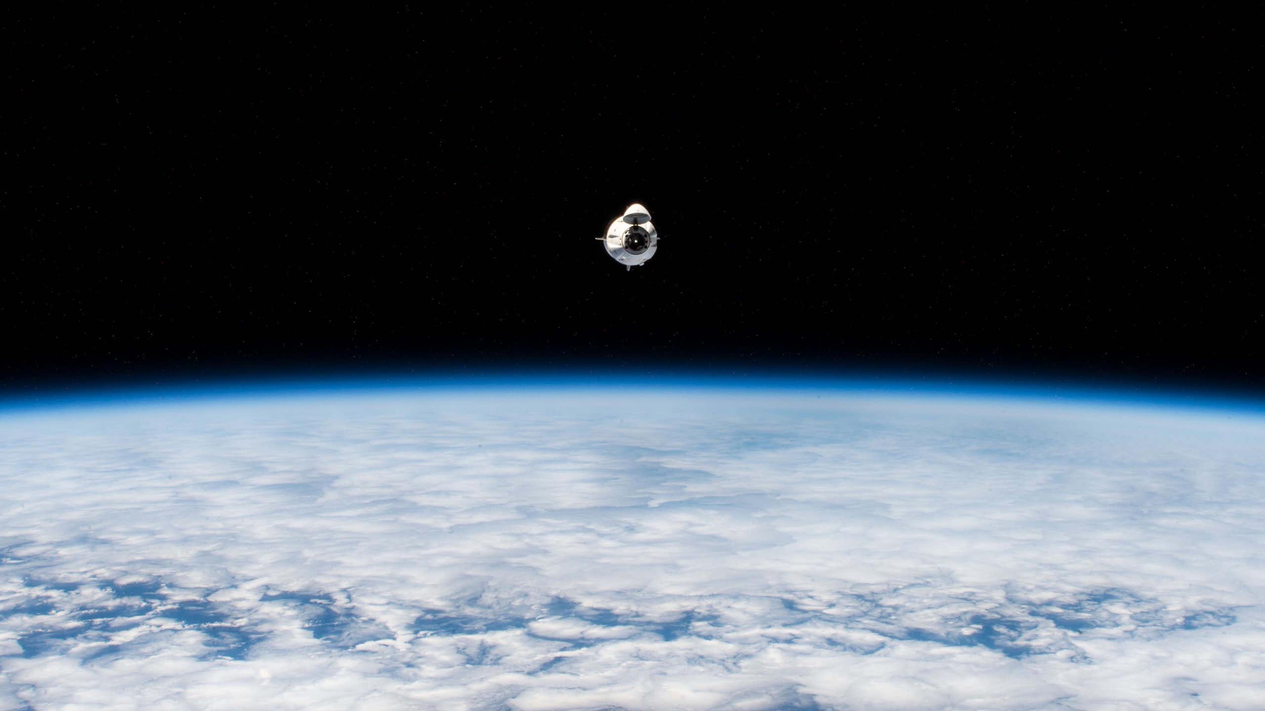 A small white capsule flying above a blue planet against a black void.