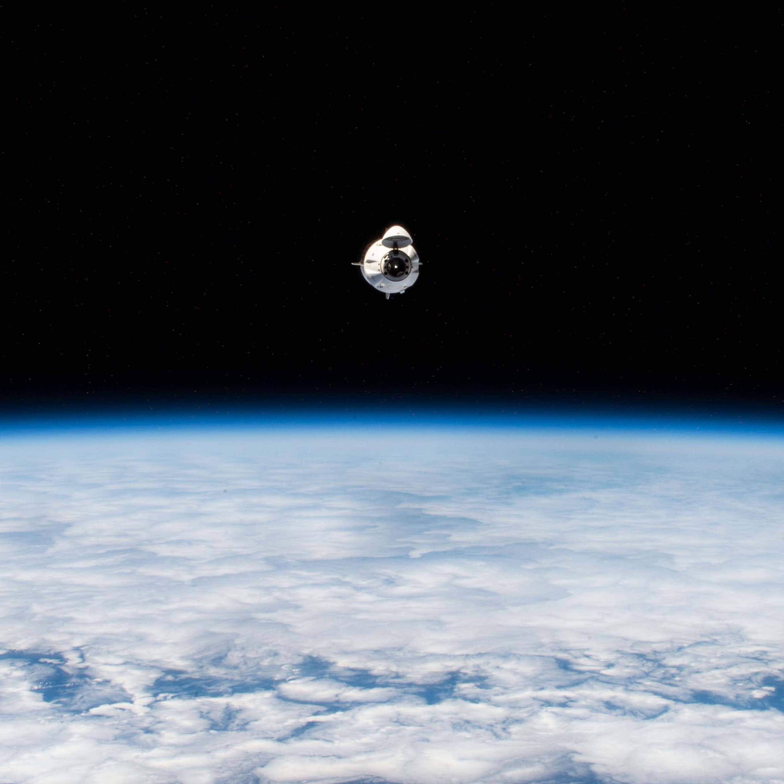 A small white capsule flying above a blue planet against a black void.