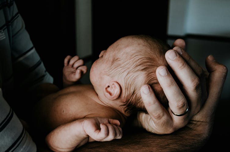 A man cradles a newborn baby.