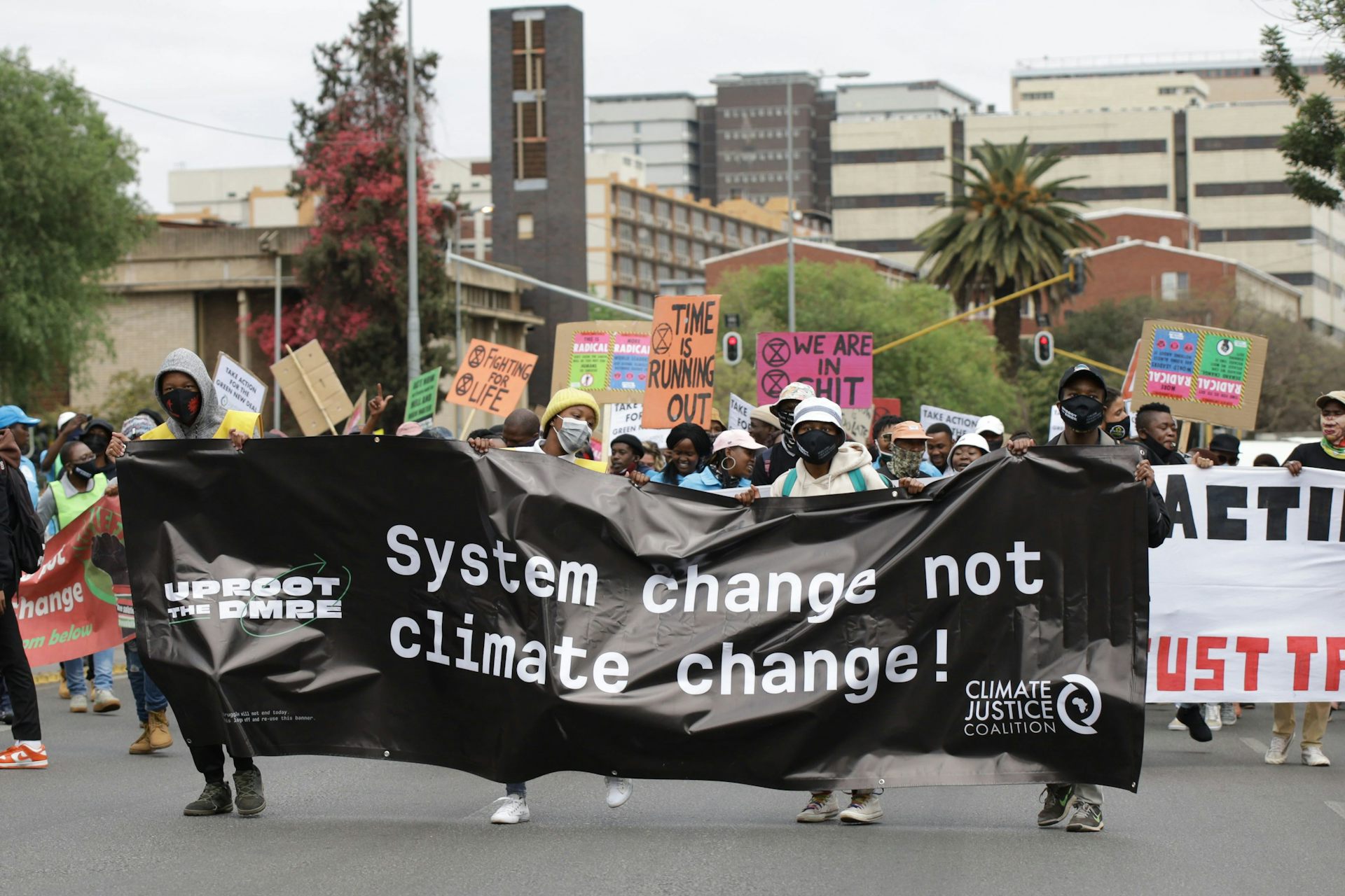 A group of a few hundred people march down a city street, carrying a banner that says 'System change not climate change'