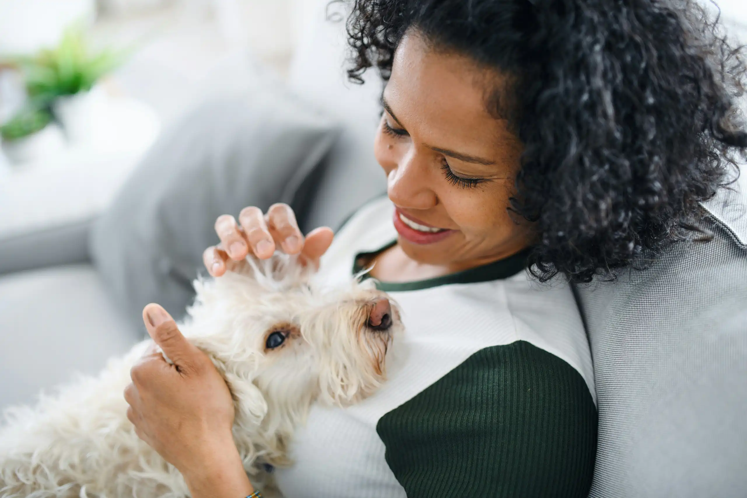 A woman sitting on a sofa with a small affectionate white dog