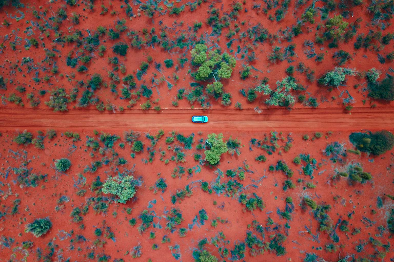 Aerial shot of car on remote red dirt road, red dirt landscape with trees