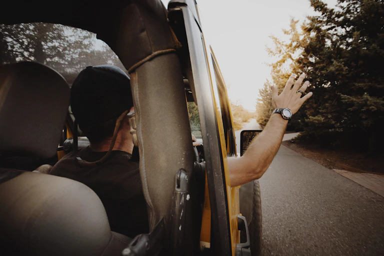 A driver holds their hand out the right side window of a car, in a waving gesture.