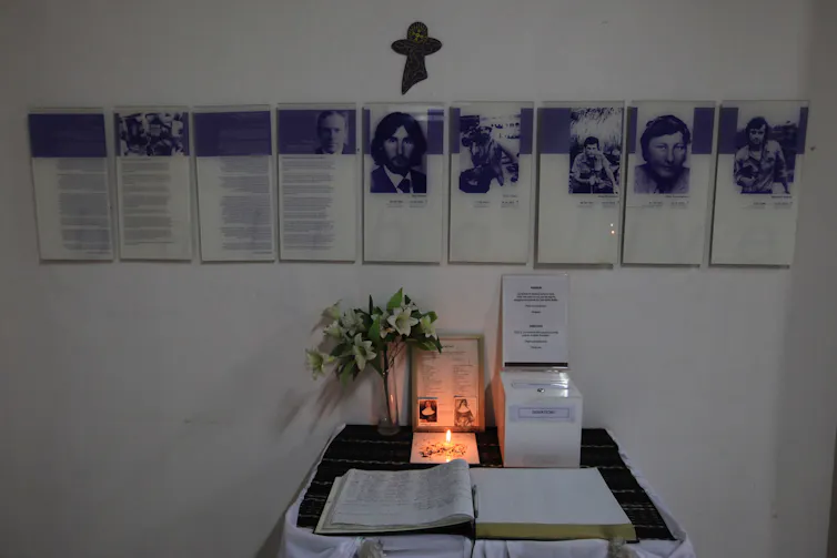 A wall with plaques memorialising men, with a candle lit in front.
