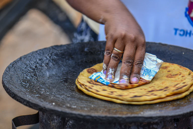 A hand cooking a flat bread on a pan on a fire.