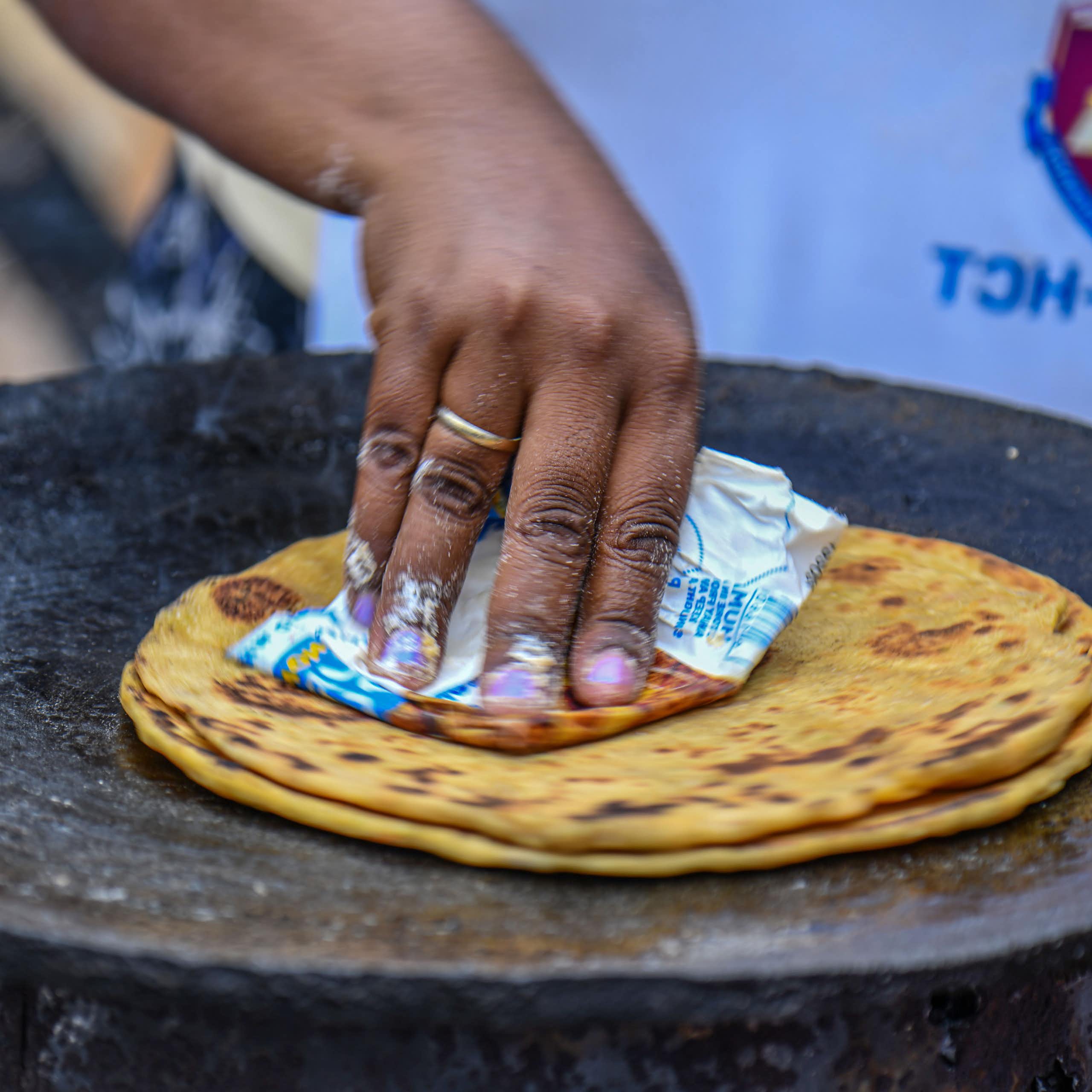 A hand cooking a flat bread on a pan on a fire.