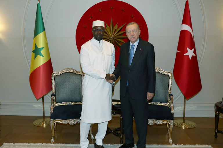 Two men shake hands, flanked by flags