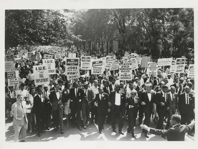 Black an white shot of a crowd of people carrying placards with Martin Luther King in the front rank.
