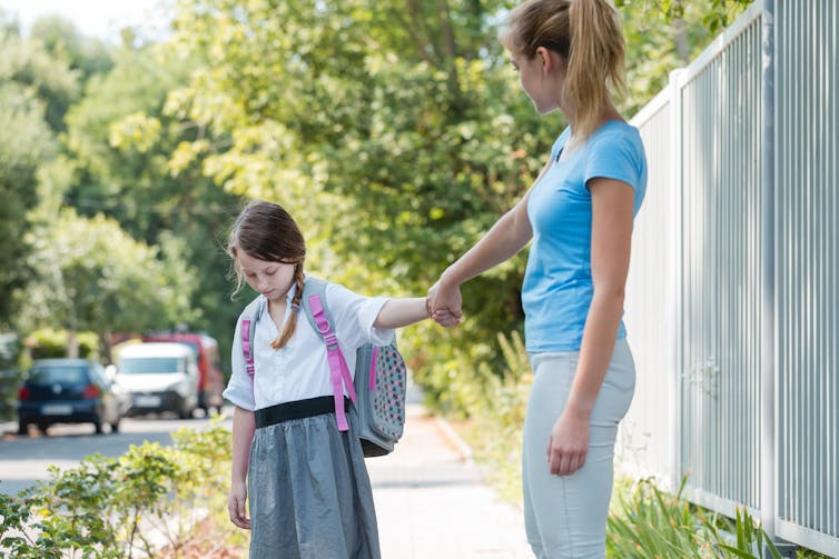 Girl holding mother's hand doesn't want to go to school
