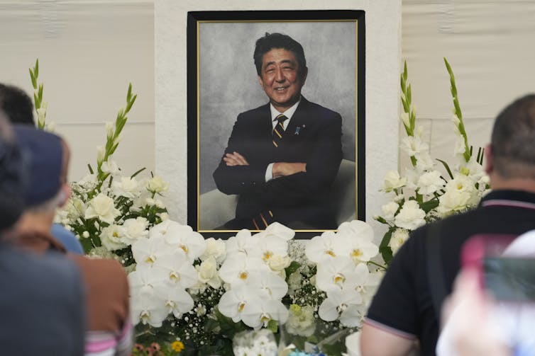 11 años después del tiroteo en Parliament Hill, ¿Canadá está haciendo lo suficiente para combatir la violencia política? 2 Retrato de un hombre asiático detrás de bancos de flores blancas con gente en primer plano.
