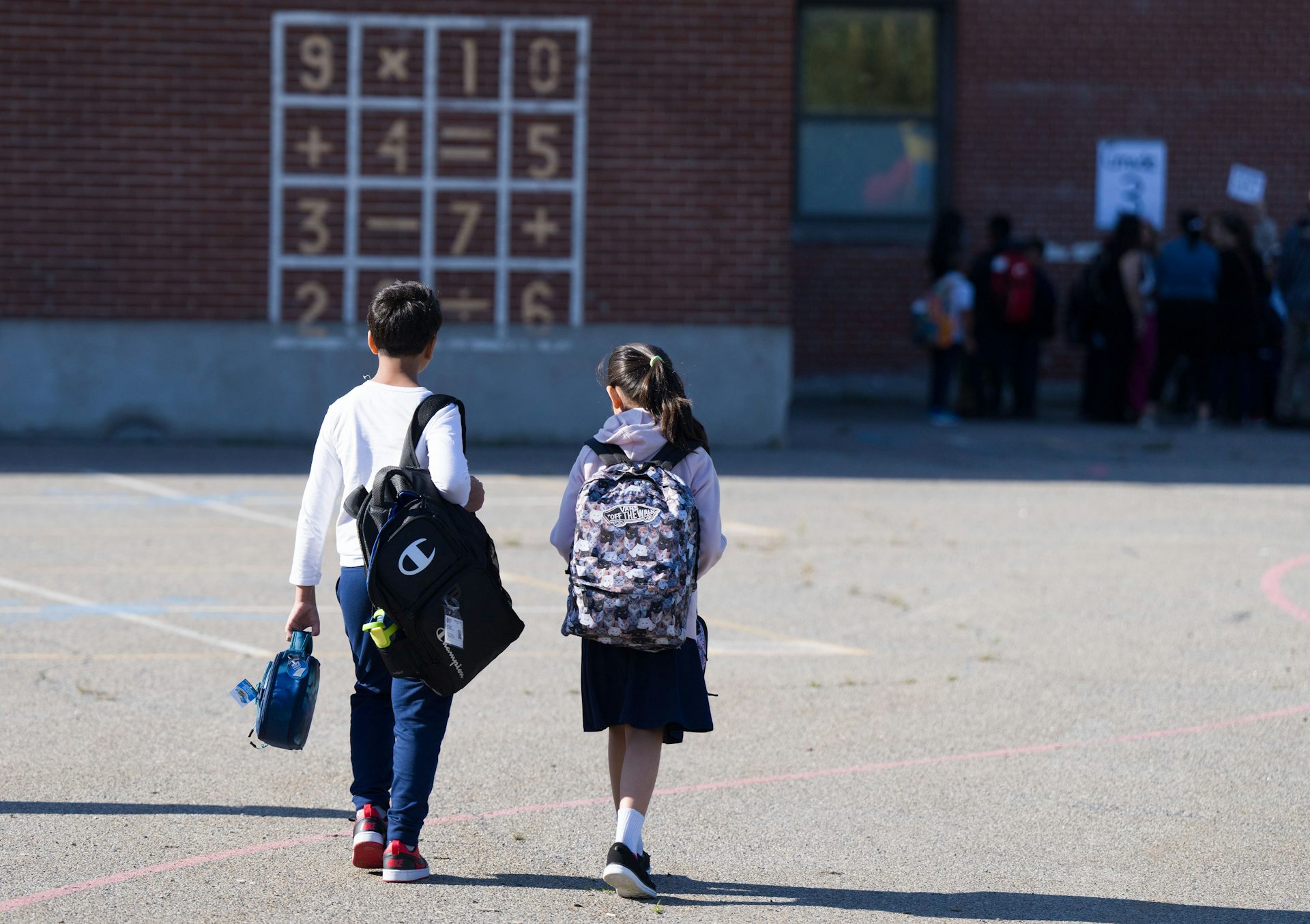 The backs of two children as they walk towards a school.