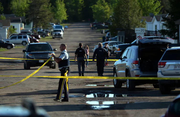 Police vehicles on a road behind yellow police tape.
