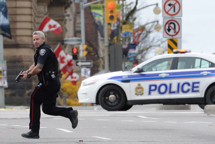 A police officer runs on a city street with his gun drawn.