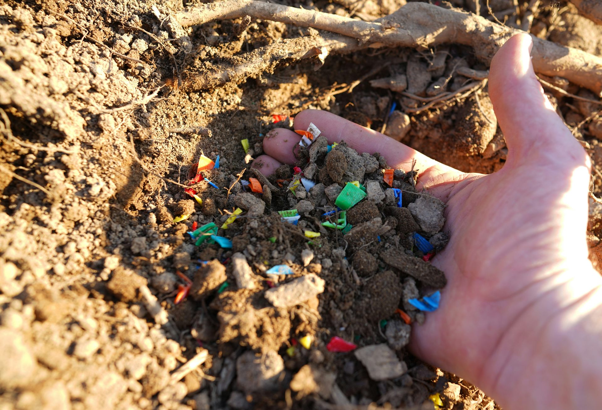 Una mano recoge microplásticos de colores de la tierra
