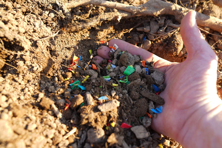 Una mano recoge microplásticos de colores de la tierra