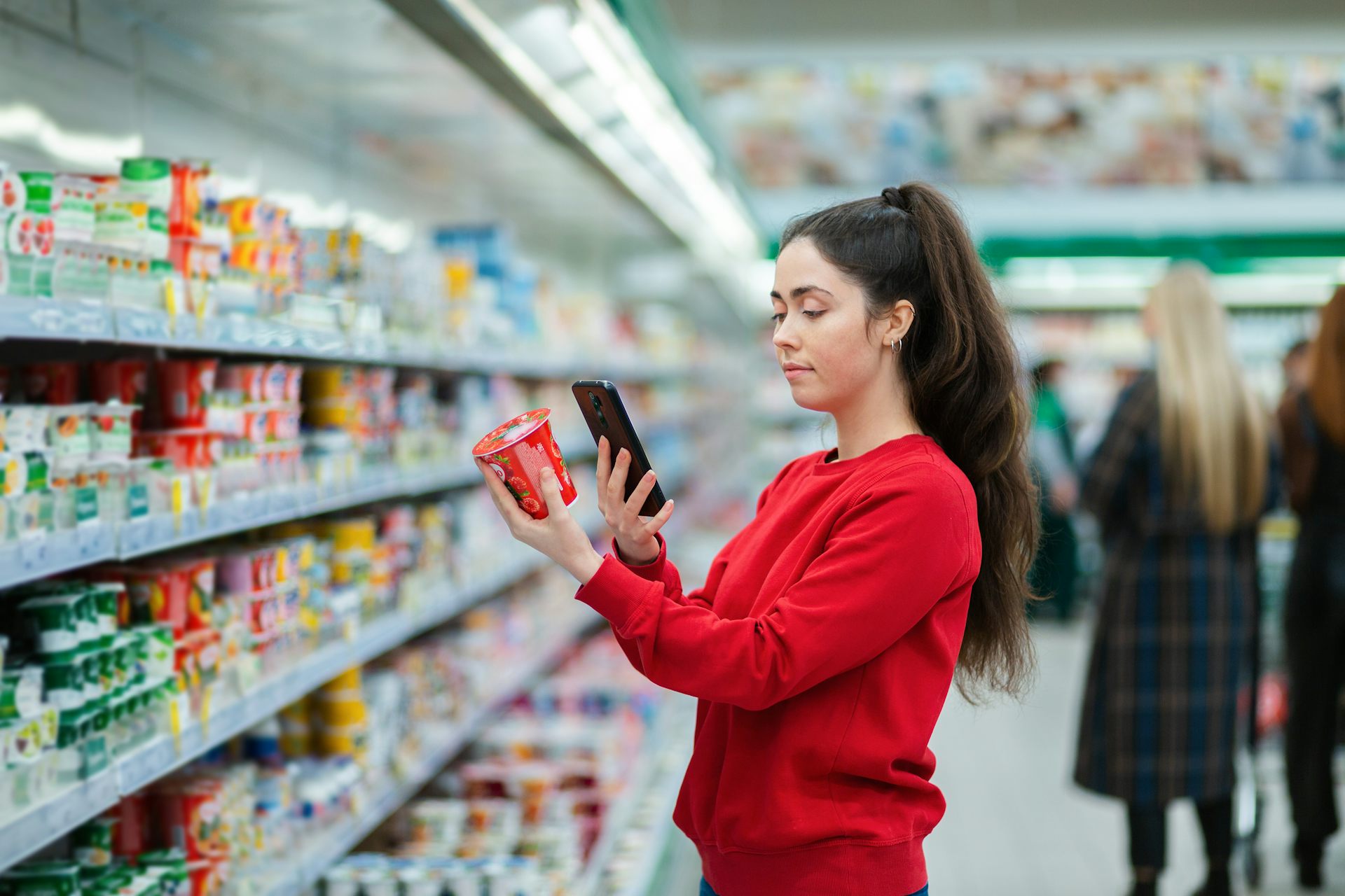 Une jeune femme scanne l’emballage d’un pot de yaourt dans le rayon d’un supermarché.