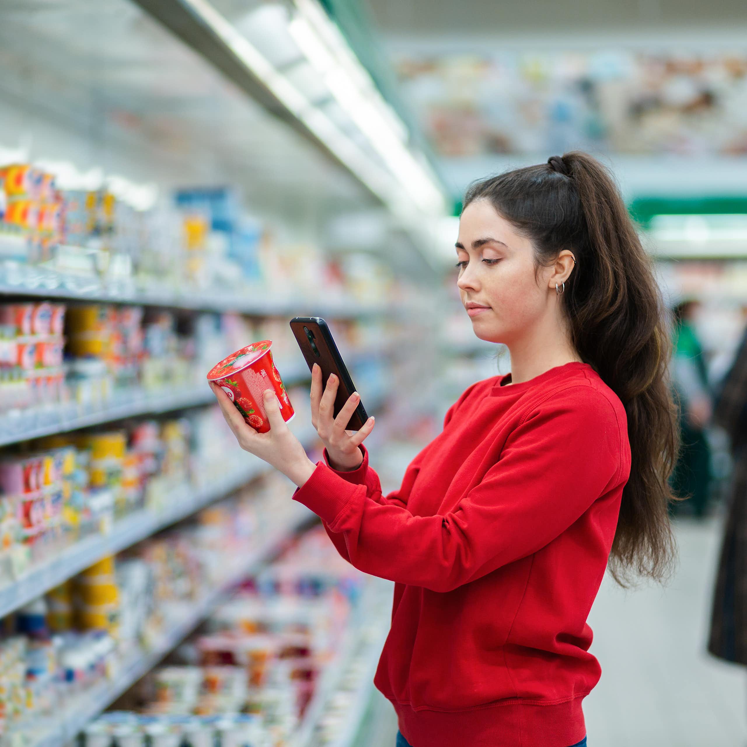 Une jeune femme scanne l’emballage d’un pot de yaourt dans le rayon d’un supermarché.