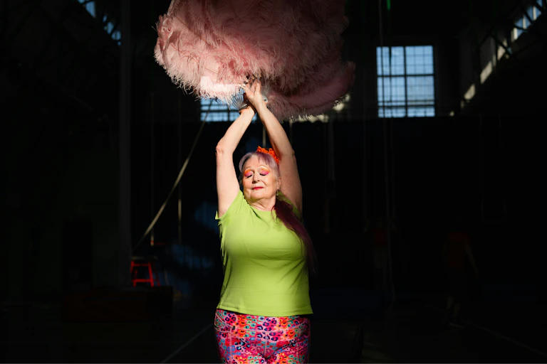 Uma mulher segurando penas cor-de-rosa, dançando.