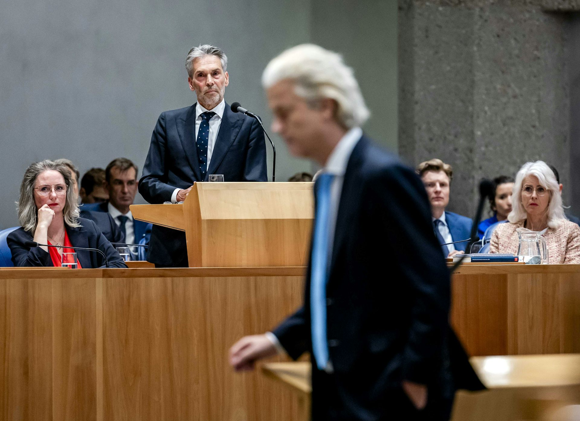 Geert WIlders walks through parliament while prime minister Dick Schoof gives a speech in the background. 