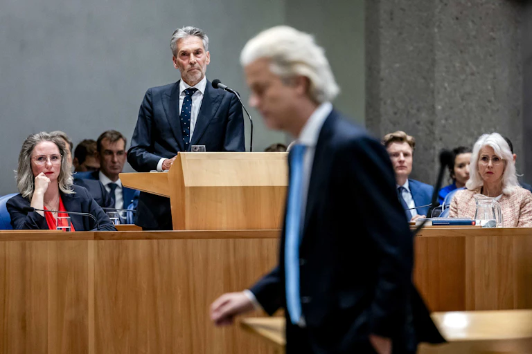 Geert WIlders walks through parliament while prime minister Dick Schoof gives a speech in the background.