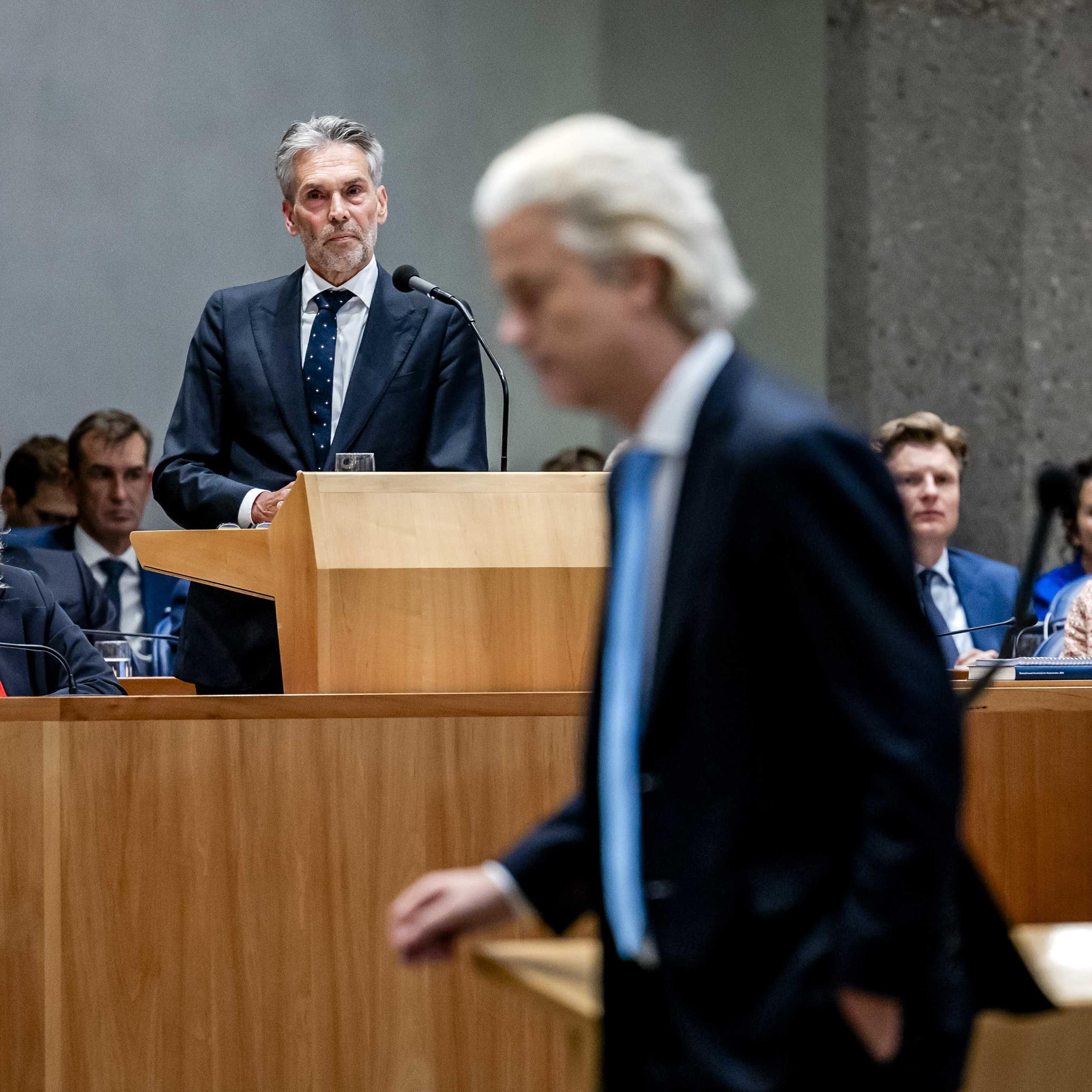 Geert WIlders walks through parliament while prime minister Dick Schoof gives a speech in the background.