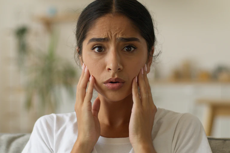 Woman with open mouth looking confused hands touching her face