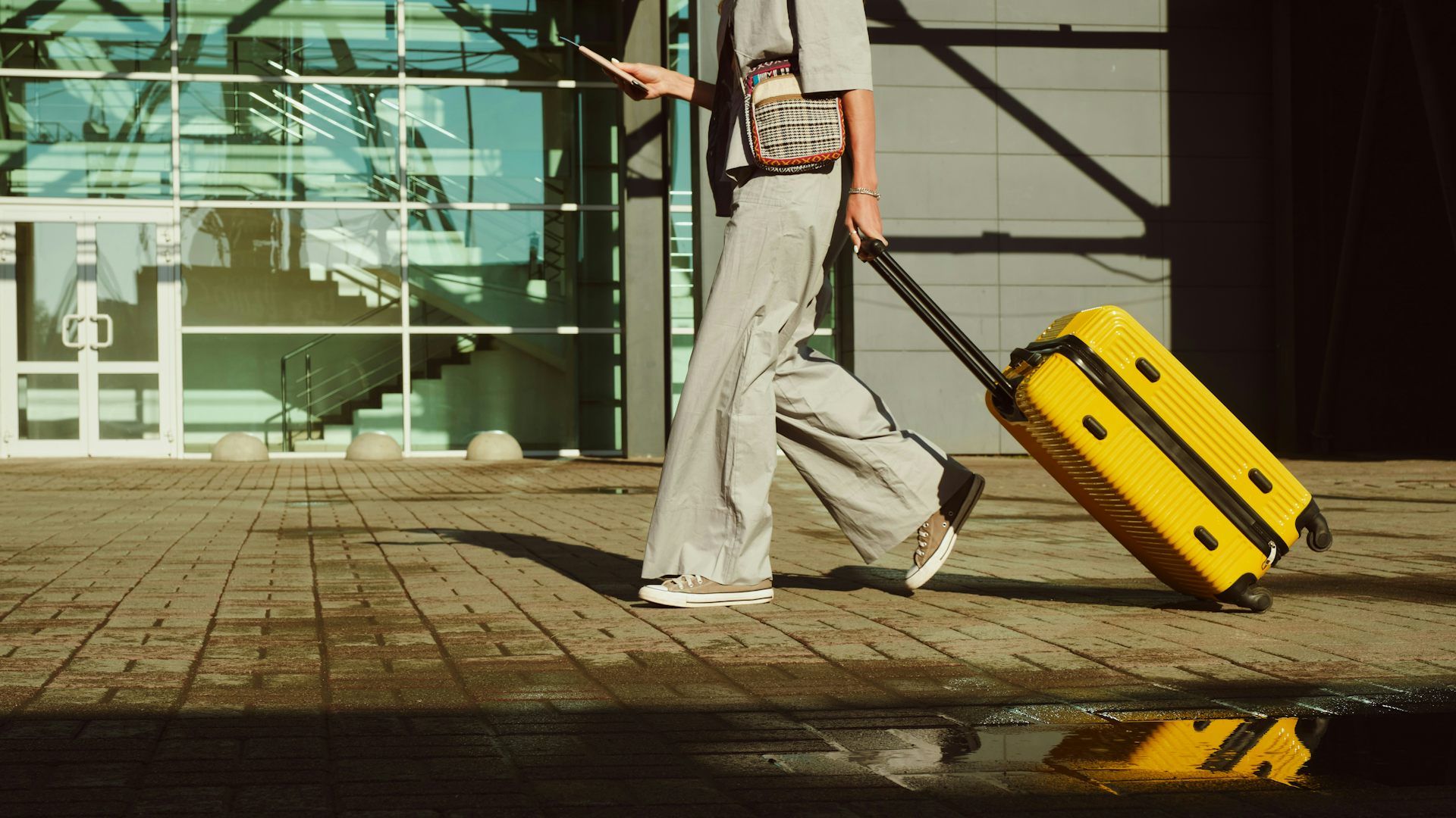Une femme vue de la taille aux pieds tirant un bagage à main jaune dans un aéroport.