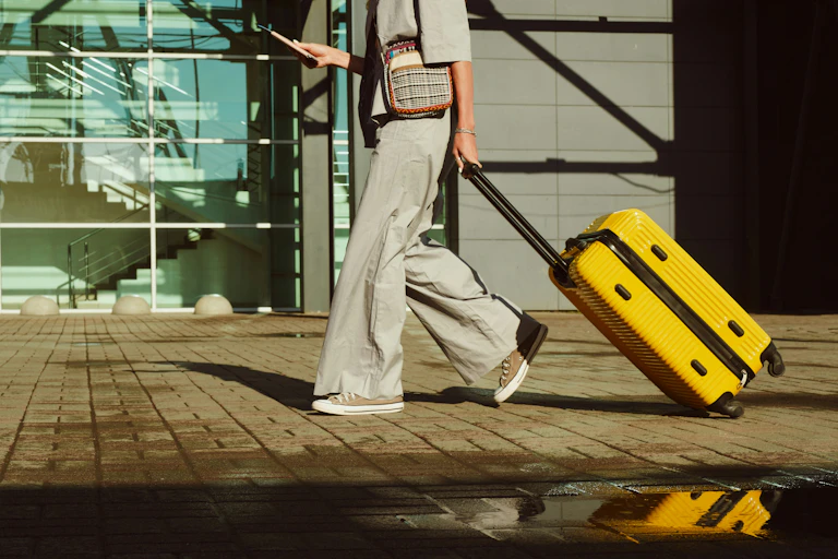 Une femme vue de la taille aux pieds tirant un bagage à main jaune dans un aéroport.