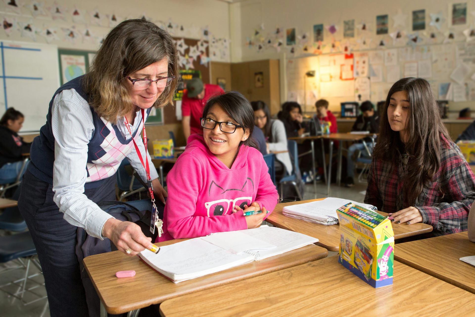 Students working at desks and a teacher is looking at one of their books.