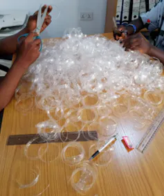 A table with dozens of shredded plastic bottles and two people with scissors cutting bottles up